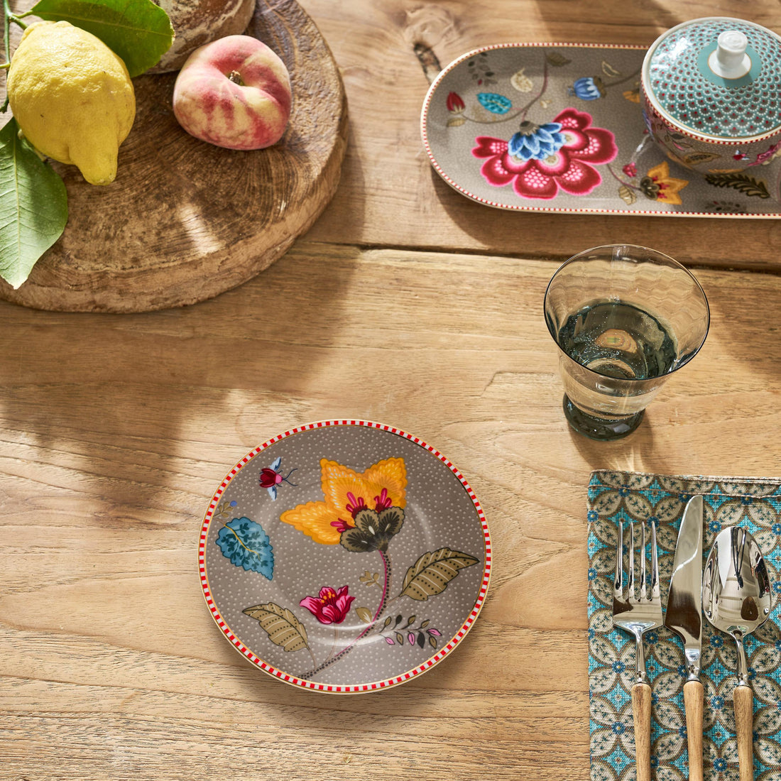 Decorative plates with floral designs on a wooden table with cutlery and a glass.