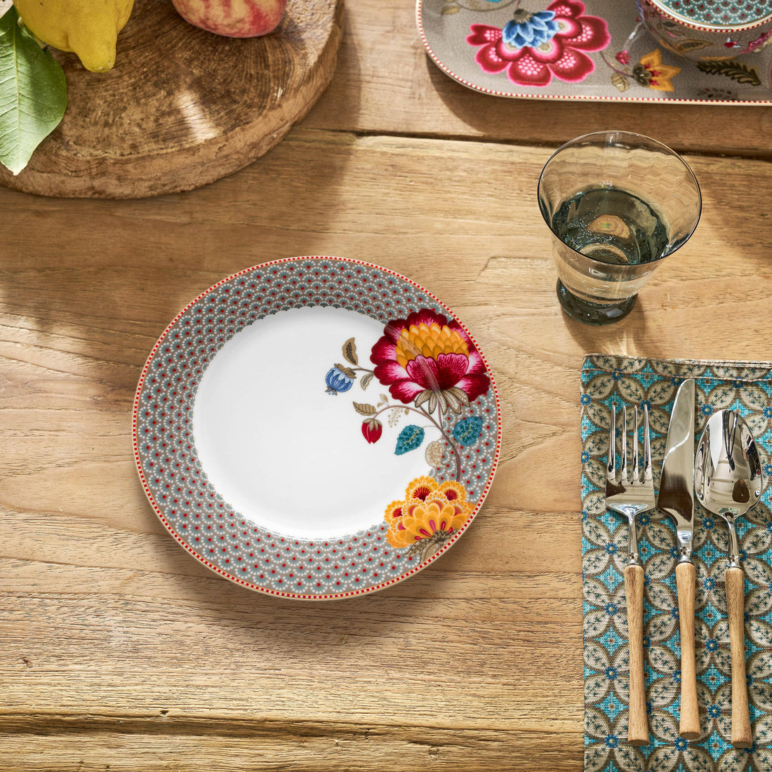 Dining table setting with floral plate, cutlery, and decorative items on a wooden surface.