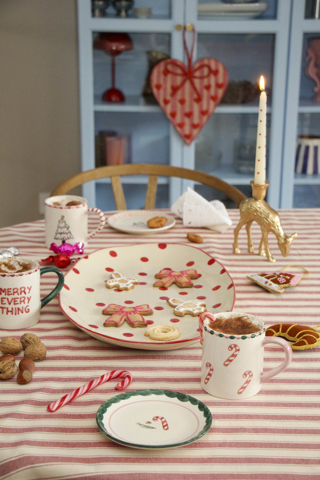 Rice kerst gebaksbordje met candy cane motief en een zuurstok naast een bijpassende mok op een rood gestreept tafelkleed.
