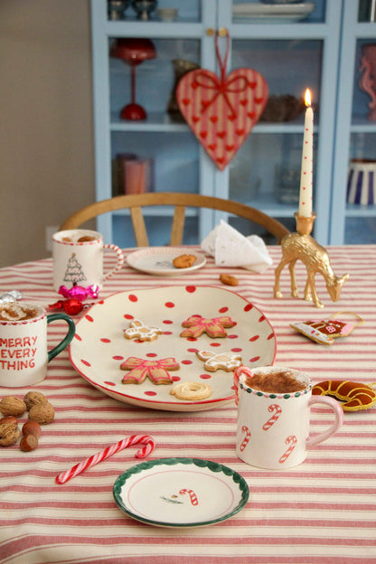 Rice kerst gebaksbordje met candy cane motief en een zuurstok naast een bijpassende mok op een rood gestreept tafelkleed.