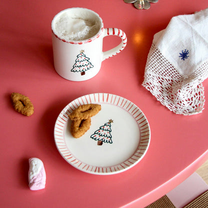 Rice kerst gebaksbordje met kerstboom en koekjes naast een bijpassende mok op een rode tafel.